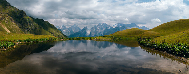 Koruldi lakes in Caucasus mountains, Mestia, Svaneti region, Georgia. Summer day, green hills, high mountain pasture for livestock, snow mountain peaks. Large panorama with high resolution