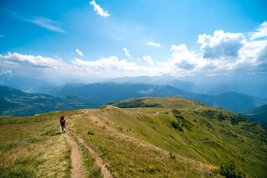 Woman at distance. dressed in wide sun hat and backpack, tourist on hiking route to Koruldi Lakes, Svaneti region, Mestia Georgia. The concept of travel and active recreation. Summer day