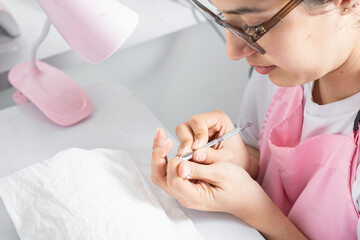 close-up of a young woman getting a manicure, removing excess nail polish with the cuticle pusher - obrazy, fototapety, plakaty