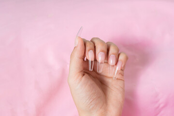 hand of a young woman on a pink background, with transparent false nails ready for a manicure