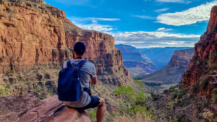 Rear view of man with backpack sitting on rock along Bright Angel trail with aerial overlook of South Rim of Grand Canyon National Park, Arizona, USA, America. Amazing vista after sunrise in summer © Chris