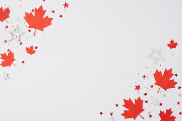 July 1st Canada Day celebration concept. Top view arrangement of red maple leaves, shiny patriotic confetti on white background with empty space for promotion or greeting