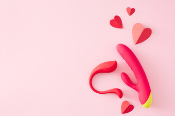 Concept of erotic pleasure toys. Top view flat lay of pink vibrator, anal plug, red hearts on pastel pink background with empty space for text or promotional purposes