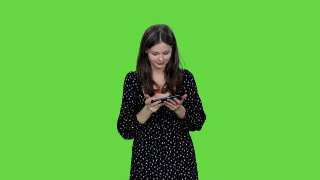 Smiling girl in polka dot dress taking selfie with smartphone on green background, Chroma key, 4k pre-keyed footage