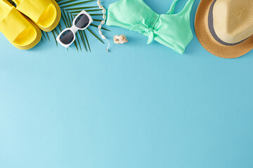 Theme of a summer journey. Top view flat lay of teal swimsuit, sunglasses, straw hat, palm leaf, yellow flip flops, seashell, shell bracelet on pastel blue background with empty space for ad or text