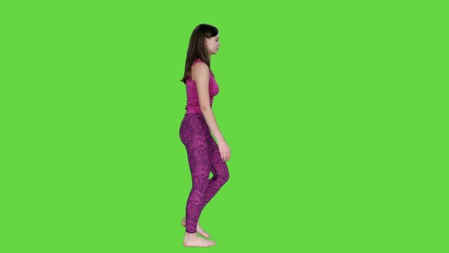 Side view of young woman in sportswear walking barefoot on green background, Chroma key