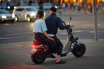 Man and woman riding electric bike in the city. Couple enjoy an evening ride on an electric scooter...
