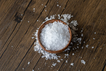 Fototapeta na wymiar Wooden bowl filled with salt flakes on wooden table with salt on it