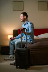 Handsome guy looking in window sitting on bed in hotel room