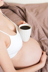 pregnant young woman sitting on bed and drinking coffee at home. maternity concept