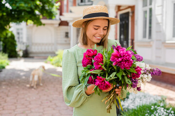 Fototapeta premium beautiful young woman in summer style outfit smiling happy walking with flowers in city street