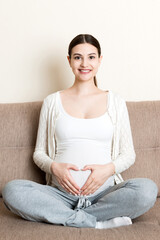 Obraz premium photo of cute caucasian future mom lying in light living room on sofa and holding hands on tummy