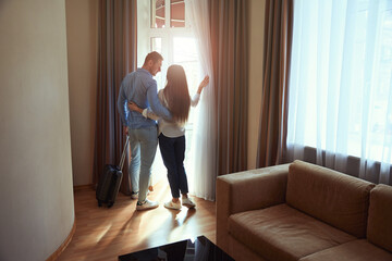 Man and a woman hugging look in window in hotel room