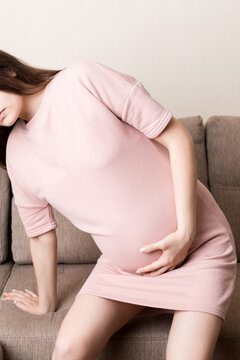 Pregnant Lady Having Massaging Lower belly Sitting On Sofa Indoor. Pregnancy Problems Concept. Maternity healthcare