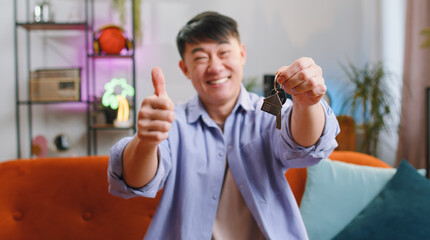 Asian man real estate agent lifting hand showing the keys of new home house apartment, buying or renting property, mortgage loan at modern home apartment indoors. Chinese guy in room. Selective focus