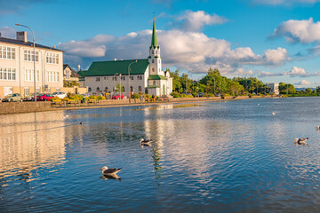 Historical and touristic downtown in Reykjavik at sunset in Iceland. Cityscape at golden hour and blue sky at inner lake around Tjornin city park in the downtown. - obrazy, fototapety, plakaty