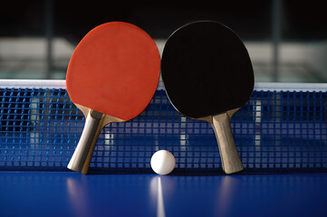 Pair of racket and ball on tennis table against grid net in sport hall