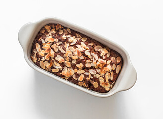 Banana cake with chocolate and almond petals in a ceramic baking dish on a light background, top view