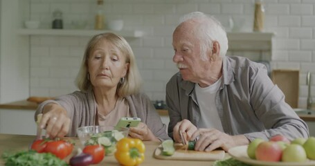 Man and woman senior couple cooking salad and checking recipe with smartphone in kitchen at home. Nutrition and modern technology concept. - Powered by Adobe