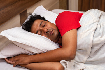 Side view of clean shaved Indian man sleeping on bed in bedroom.