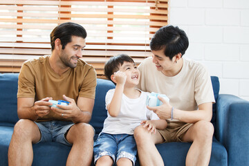 Lovely little boy gives fathers a present in the father's day festival, happy Asian and Caucasian gay couple with foster son. A diversity in gender - LGBTQ and ethnicity concept.
