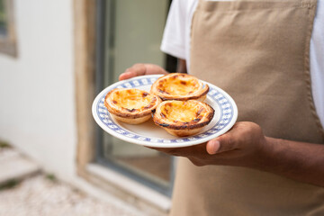 Young African man waiter serving 
 a plate with Portugal's traditional sweet dessert Pastel de...