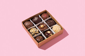Gift box with chocolate craft candies with nuts inside on pink background