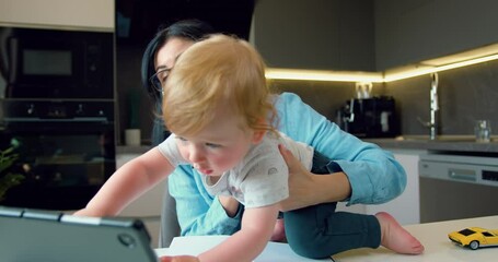 Business woman working online, useing digital tablet and having video call with partners, her little son is sitting next to her, who interferes with her mother's work. - Powered by Adobe