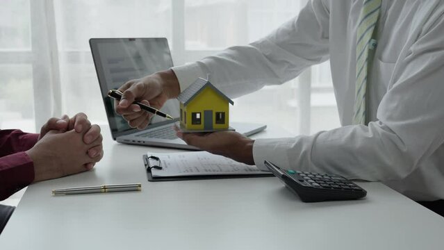real estate agent assisting client to sign contract paper at desk with house model, house agency and insurance concept.