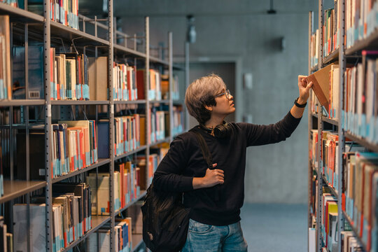 Portrait of asian student picking book from bookshelf in library
