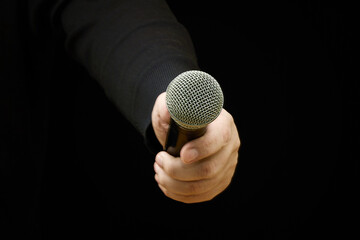 Hand holding out microphone for interview close-up on dark background..