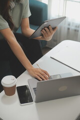 Happy Asian teen girl holding pad computer gadget using digital tablet technology sitting on the couch at home. Smiling young woman using apps, shopping online, reading news, browsing internet on sofa