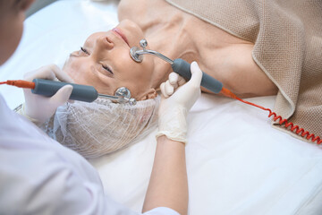 Cosmetician doing microcurrent therapy on client's face in modern clinic