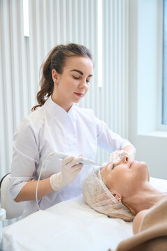 Happy beautician making cosmetic facial cleansing for adult lady