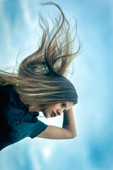Modern young woman wearing casual outfit with hair loose and blowing in the wind on serene afternoon with beautiful sky.