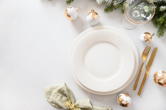 Beautiful Christmas festive table setting with white plate, golden balls on white.