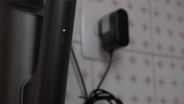 charging light on appliance in its charging base, next to a plug and its electric charger
