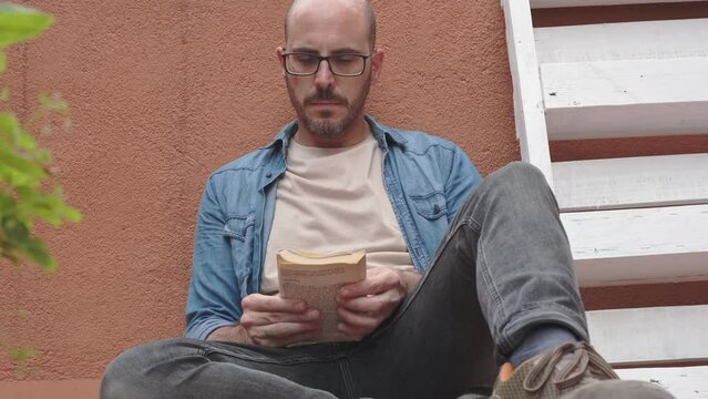 middle-aged man reading book on the floor of his terrace
