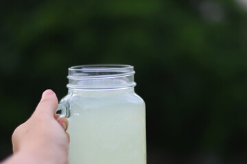 Hand holding a glass of lemonade outdoor. Selective focus.