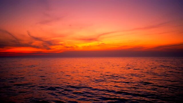 Beautiful sea waves with reflection of red and orange, sunset light glowing, by the beach with colorful yellow sky clouds on the background, calm horizon scene, wide shot, slow motion. ProRes 422 HQ