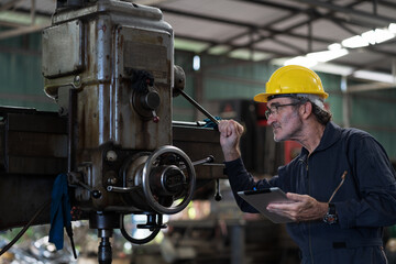 Senior male engineer worker working and inspecting parts quality of lathe machine in industry factory, wearing safety uniform, helmet. Mature male technician worker maintenance parts of machine