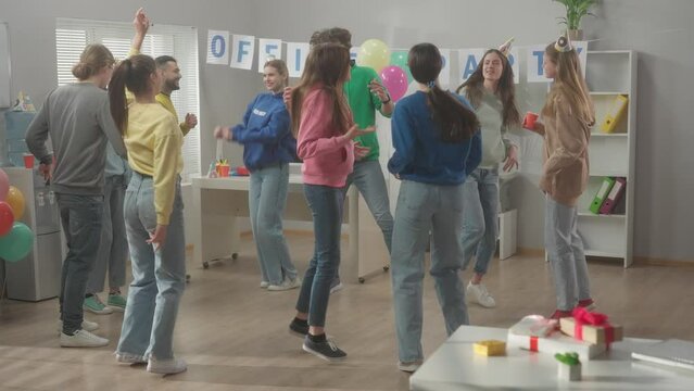 Employees have fun in the office. The team celebrate the common success, dance. The interior of the office is decorated with inscription OFFICE PARTY. Slow motion. HDR BT2020 HLG Material.