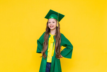 The child is a graduate. A little girl in a graduate hat on a yellow isolated background. Happy...