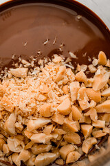 Melted chocolate and chopped peanuts in transparent measuring cup on white kitchen table. Closeup view