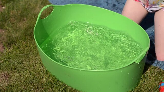 The child splashes in the basin of water. Summer water fun and games