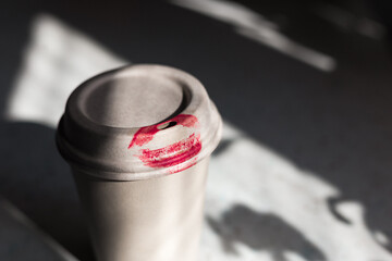 Paper cup with red lipstick kiss print on the table. Pink woman  lips marks.