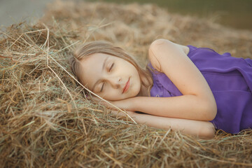 Naklejka na ściany i meble Young pretty girl teenager sleeping with hands under her head on a yellow haystack on a farm in countryside, warm summer outdoor lifestyle kid's portrait, idea of leisure, carefree resting and peace