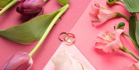 Wedding rings with beautiful flowers on color background