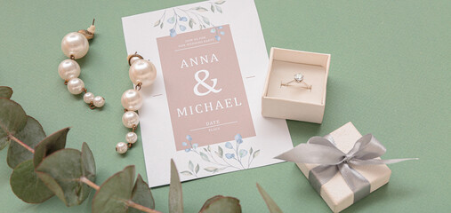 Box with engagement ring, earrings and wedding invitation on green background