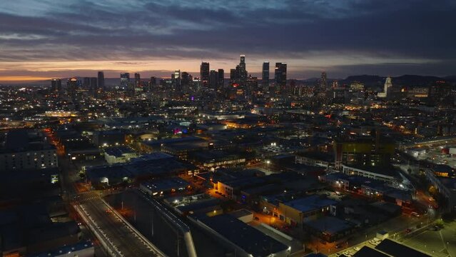 Fly above night city. Aerial panoramic view of buildings in urban borough and skyscrapers in background. Los Angeles, California, USA